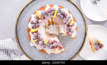 Flach liegend. Schritt für Schritt. Schneiden von Zitrone Cranberry Bundt Kuchen mit Zucker Cranberries und Zitronenkeile verziert. Stockfoto