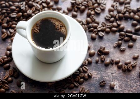 Weiße Tasse mit starkem schwarzen Kaffee auf einem rustikalen Holztisch mit einigen Bohnen, Kopierraum, ausgewählter Fokus, enge Schärfentiefe Stockfoto