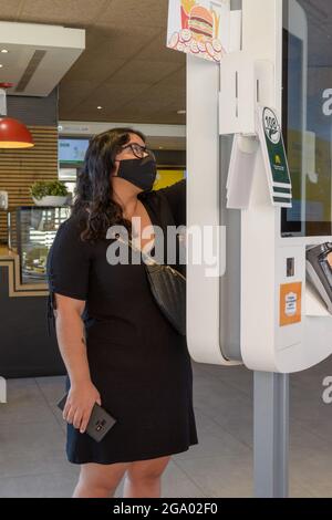 Mallorca, Spanien, 07-27-2021: Junge Frau, die in Macdonalds Fast-Food-Restaurant in der Zeit nach der Pandemie eine Bestellung über einen Touchscreen mit Maske aufgab, Stockfoto