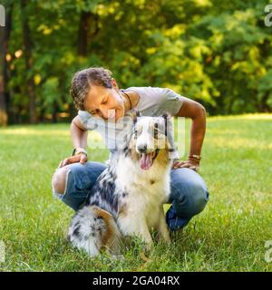 Glückliche junge Frau, die am Sommertag Zeit mit einem lieblich gefleckten australischen Schäferhund auf einer grünen Wiese verbringt Stockfoto