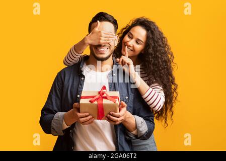 Überraschungsgeschenk. Romantische junge arabische Frau, die die Augen des Freundes bedeckt und Geschenke macht Stockfoto