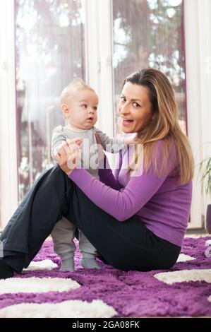 Glückliche Mutter, die auf dem Boden sitzt und mit ihrem kleinen Jungen spielt Stockfoto