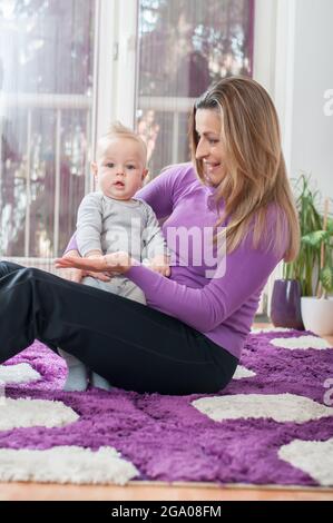 Glückliche Mutter, die auf dem Boden sitzt und mit ihrem kleinen Jungen spielt Stockfoto