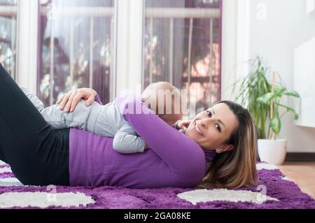 Glückliche Mutter, die sich auf den Boden legt und mit ihrem kleinen Jungen spielt Stockfoto