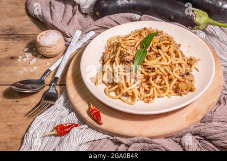 Traditionelle sizilianische Pasta-Gericht aus sautierten Auberginen mit Tomatensauce gekrönt. Das Essen wird auf einem Keramikplatte serviert, italienische Küche, modernes hartes Licht, dunkel Stockfoto