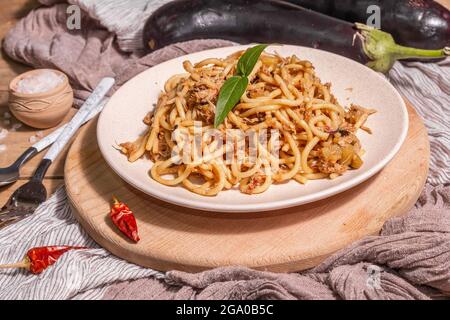 Traditionelle sizilianische Pasta-Gericht aus sautierten Auberginen mit Tomatensauce gekrönt. Das Essen wird auf einem Keramikplatte serviert, italienische Küche, modernes hartes Licht, dunkel Stockfoto