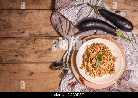 Traditionelle sizilianische Pasta-Gericht aus sautierten Auberginen mit Tomatensauce gekrönt. Das Essen wird auf einem Keramikplatte serviert, italienische Küche, modernes hartes Licht, dunkel Stockfoto