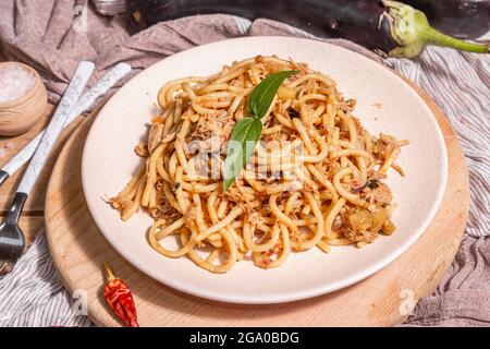 Traditionelle sizilianische Pasta-Gericht aus sautierten Auberginen mit Tomatensauce gekrönt. Das Essen wird auf einem Keramikplatte serviert, italienische Küche, modernes hartes Licht, dunkel Stockfoto