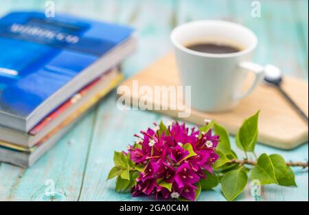 Nahaufnahme von rosa Blumen mit Büchern und einer Tasse Kaffee im Hintergrund Stockfoto