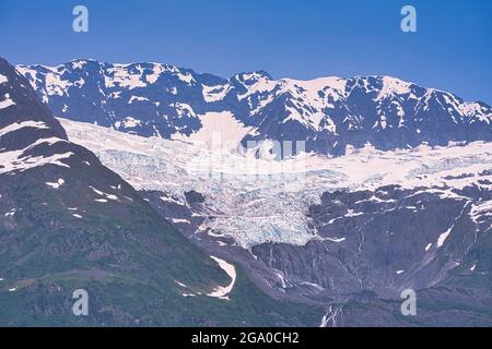 Im Sommer wird der Gletscher von dunklen, felsigen Bergen flankiert. Genießen Sie den Blick auf das Schelfeis vom Schiff aus. Alaska, USA. Juli 2019. Stockfoto