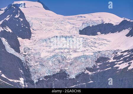 Im Sommer wird der Gletscher von dunklen, felsigen Bergen flankiert. Genießen Sie den Blick auf das Schelfeis vom Schiff aus. Alaska, USA. Juli 2019. Stockfoto