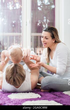 Glückliche Eltern, die auf dem Boden liegen und sitzen und mit ihrem Jungen spielen. Vater hält sein Kind. Stockfoto