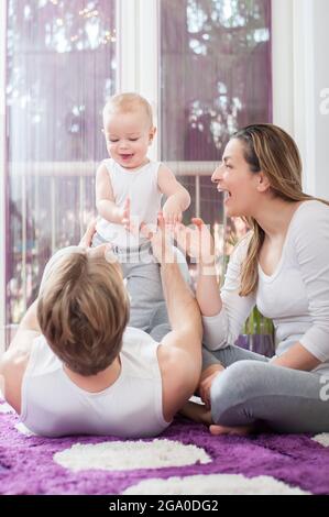 Glückliche Eltern, die auf dem Boden liegen und sitzen und mit ihrem Jungen spielen. Vater hält sein Kind. Stockfoto