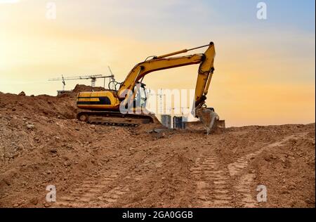 Bagger gräbt Schmutz bei Straßenarbeiten auf der Baustelle. Schwere Maschinen und Erdbewegungsmaschinen im Straßenbau. Turmdrehkrane in Aktion auf s Stockfoto