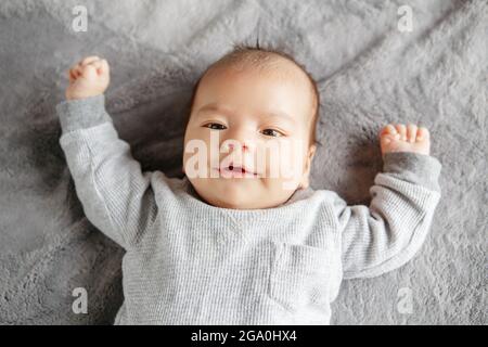 Süßes kleines zwei Monate neugeborenes asiatisches chinesisches Baby, das auf seinem Rücken liegt. Wake Wake Aware Baby Junge Blick auf die Kamera. Blick von oben Stockfoto