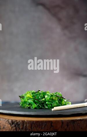 Wakame-Algensalat mit Sesam auf schwarzem Teller und Holztisch Stockfoto