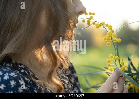 Nahaufnahme Porträt einer sanften schönen jungen glücklich geheimnisvoll inspiriert Frau Brünette mit langen Haaren lächelnd lachend mit einem blühenden Akazienbaum Stockfoto