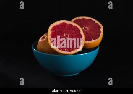 Rote Grapefruit in blauer Schale auf schwarzem Hintergrund Stockfoto