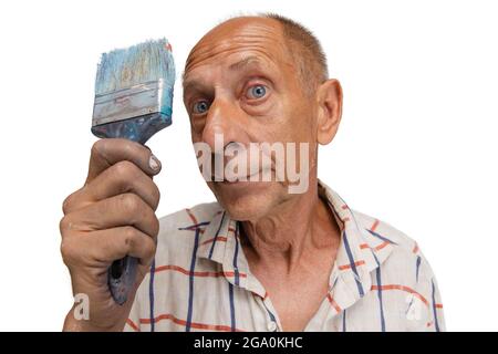 Ältere oder ältere Graumaler mit einem Pinsel, der vor der Kamera steht. Lustiger Mann in einem bemalten Hemd, der isoliert auf Weiß herumtollt Stockfoto