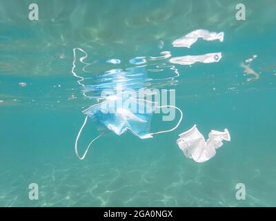 Ausrangierte chirurgische Gesichtsmaske und Plastikbecher auf kontaminiertem Meeresökosystem schwimmend, kovid19 Umweltverschmutzung Stockfoto