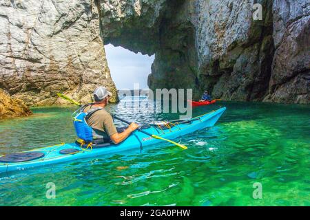 Erkunden Sie Meereshöhlen, während Sie vor der Küste von Anglesey, Nordwales, Großbritannien, Kajakfahren Stockfoto