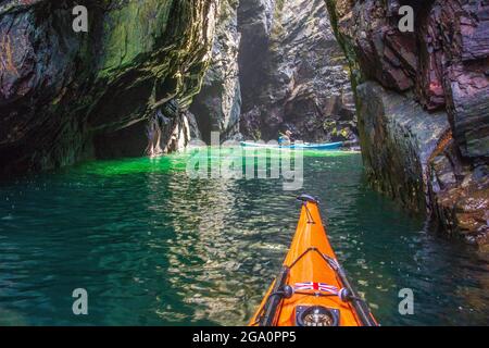 Erkunden Sie Meereshöhlen, während Sie vor der Küste von Anglesey, Nordwales, Großbritannien, Kajakfahren Stockfoto