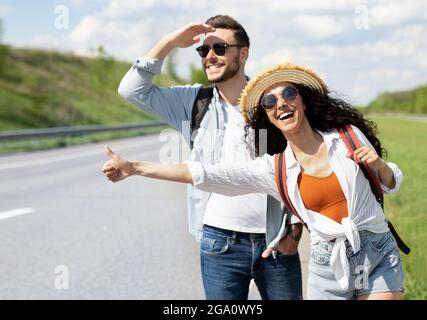 Fröhliches, junges Coupé, das das Auto herunterfährt, eine Fahrt braucht und draußen am Straßenrand unterwegs ist Stockfoto