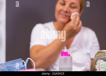 Die Pose einer Frau mit Akne-Problem auf dem Gesicht, die vor ihrer medizinischen Maske, Flasche Lotion und Wattestäbchen auf dem Tisch, so dass sie verwendet Stockfoto