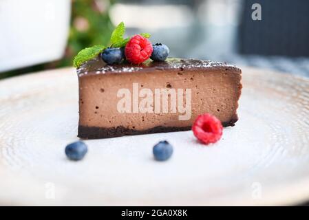 Köstlicher Schokoladendessert Käsekuchen auf einem Tisch mit Himbeeren und Heidelbeeren in einem Restaurant Stockfoto