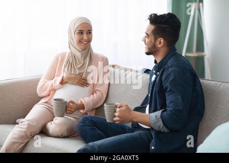 Glückliches Erwartungsfreuliches Paar Aus Dem Nahen Osten, Das Sich Zu Hause Auf Der Couch Ausruhte Stockfoto