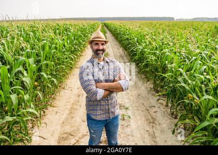 Stolzer Bauer steht in seinem wachsenden Maisfeld. Er ist zufrieden mit der erfolgreichen Saison. Stockfoto