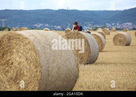 Blankenburg, Deutschland. Juli 2021. Strohballen liegen auf einem Feld im Vorland des Harzes. Ein kleiner Junge ruht auf den schweren Rollen und genießt das freundliche warme Wetter. Quelle: Matthias Bein/dpa-Zentralbild/ZB/dpa/Alamy Live News Stockfoto