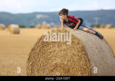 Blankenburg, Deutschland. Juli 2021. Strohballen liegen auf einem Feld im Vorland des Harzes. Ein kleiner Junge ruht auf den schweren Rollen und genießt das freundliche warme Wetter. Quelle: Matthias Bein/dpa-Zentralbild/ZB/dpa/Alamy Live News Stockfoto