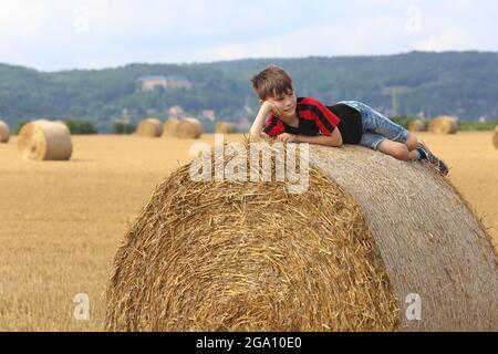 Blankenburg, Deutschland. Juli 2021. Strohballen liegen auf einem Feld im Vorland des Harzes. Ein kleiner Junge ruht auf den schweren Rollen und genießt das freundliche warme Wetter. Quelle: Matthias Bein/dpa-Zentralbild/ZB/dpa/Alamy Live News Stockfoto