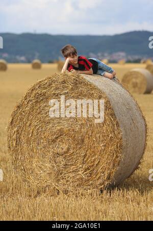 Blankenburg, Deutschland. Juli 2021. Strohballen liegen auf einem Feld im Vorland des Harzes. Ein kleiner Junge ruht auf den schweren Rollen und genießt das freundliche warme Wetter. Quelle: Matthias Bein/dpa-Zentralbild/ZB/dpa/Alamy Live News Stockfoto