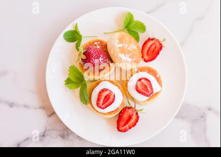 Köstliches Frühstück am Morgen. Käsepfannkuchen. Quark-Pfannkuchen, wunderschön dekoriert mit Erdbeerscheiben und saurer Creme Stockfoto