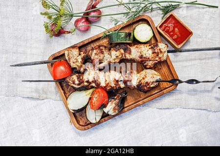 Köstlicher Kebab auf den Spiessen. Gebratenes Fleisch auf einem Holzteller. Gegrilltes Fleisch auf Spiessen. Gegrilltes Fleisch, gebackenes Gemüse und Sauce. Stillleben. Schaschlik Stockfoto