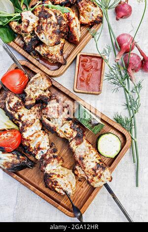 Zwei Portionen köstlicher Holzkohlensaschlik. Gebratenes Fleisch auf einem Holzteller. Gegrilltes Fleisch auf Spießen, gebackenes Gemüse und Sauce. Stillleben. Zerschmettern Stockfoto