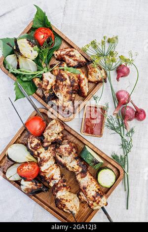 Zwei Portionen köstlicher Holzkohlensaschlik. Gebratenes Fleisch auf einem Holzteller. Gegrilltes Fleisch auf Spießen, gebackenes Gemüse und Sauce. Stillleben. Zerschmettern Stockfoto