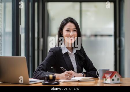 Porträt einer Geschäftsfrau und von Anwälten, die im Büro Vertragsdokumente mit Messingskala auf einem Holzschreibtisch diskutieren. Recht, Rechtsdienste, Beratung, Justiz und Stockfoto