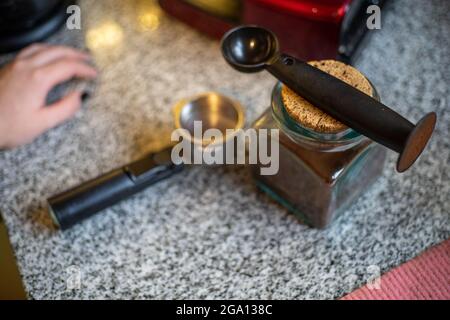 Nahaufnahme eines Glasglases mit gemahlenem Kaffee, Löffel und Portafilter auf Granitstruktur Stockfoto