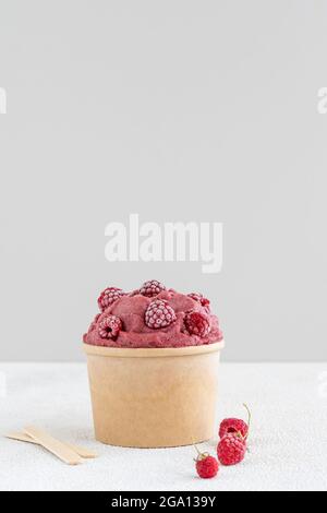 Rote Himbeere und Banane veganes Eis mit gefrorenen Himbeeren in Papierschüssel Stockfoto
