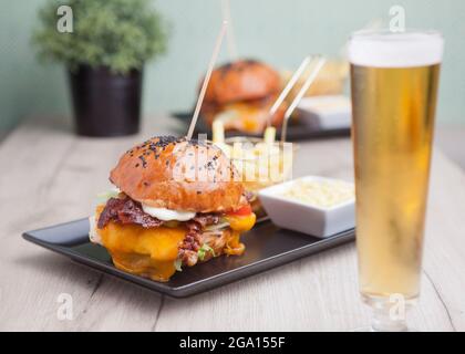 Cheeseburger mit Speck, Salat und Chips. Kalorienreiche Lebensmittel. Geschmolzener, fester, glatter Cheddar-Käse, ursprünglich hergestellt in Cheddar im Südwesten Englands. Stockfoto