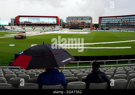 Die Zuschauer halten sich unter einem Regenschirm zurück, während der Regen den Beginn des Spiels während des 100-Matches im Emirates Old Trafford, Manchester, verzögert. Bilddatum: Mittwoch, 28. Juli 2021. Stockfoto