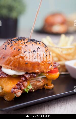 Cheeseburger mit Speck, Salat und Chips. Kalorienreiche Lebensmittel. Geschmolzener, fester, glatter Cheddar-Käse, ursprünglich hergestellt in Cheddar im Südwesten Englands. Stockfoto