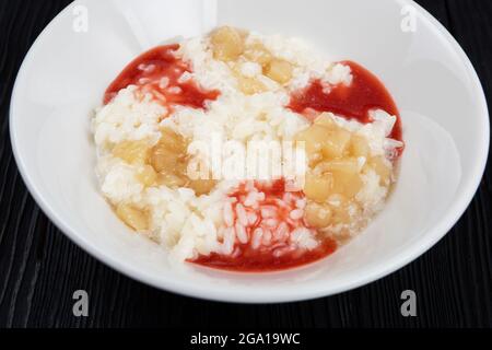 Reismilchbrei mit Erdbeermarmelade und Apfelmarmelade auf weißem Teller auf schwarzem Holzhintergrund Stockfoto