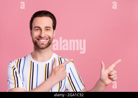 Foto Porträt Mann in gestreiften T-Shirt lächelnd zeigt Finger Copyspace isoliert pastellrosa Hintergrund Stockfoto