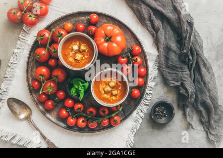 Zwei Tassen gefüllt mit frischer, hausgemachter Tomatensuppe auf einem Holztablett, Draufsicht Stockfoto