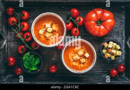 Zwei Tassen gefüllt mit frischer hausgemachter Tomatensuppe auf einem Holztablett auf Holzgrund, Draufsicht Stockfoto