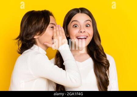 Foto-Porträt des kleinen Jungen flüsternd erstaunt fröhliche Mädchen Geheimnis auf lebendige gelbe Farbe Hintergrund isoliert Stockfoto